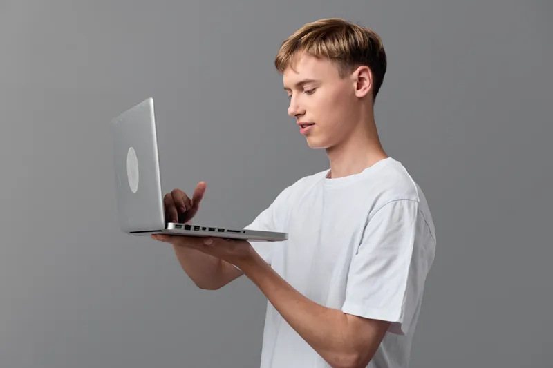 Laptop holding in one hand by a man in a white tee, capturing a focus gesture of learning, technology, and casual work in a modern studio setting