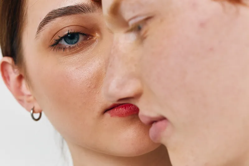 Closeup portrait of young woman and man with serious expressions on face soft focus on man with blue eyes earring and natural skin texture on white background.
