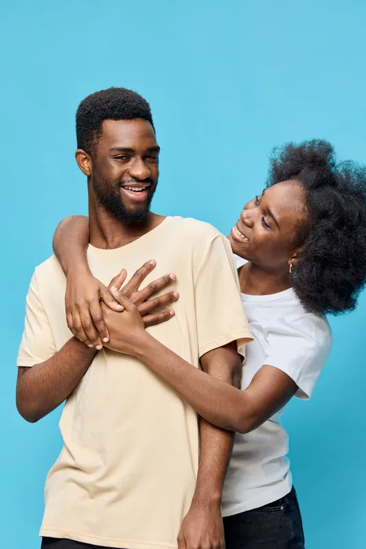 Joyful couple laughing together against a vibrant blue background, showcasing love and connection, dressed casually in light clothing, ideal for relationships and happiness themes