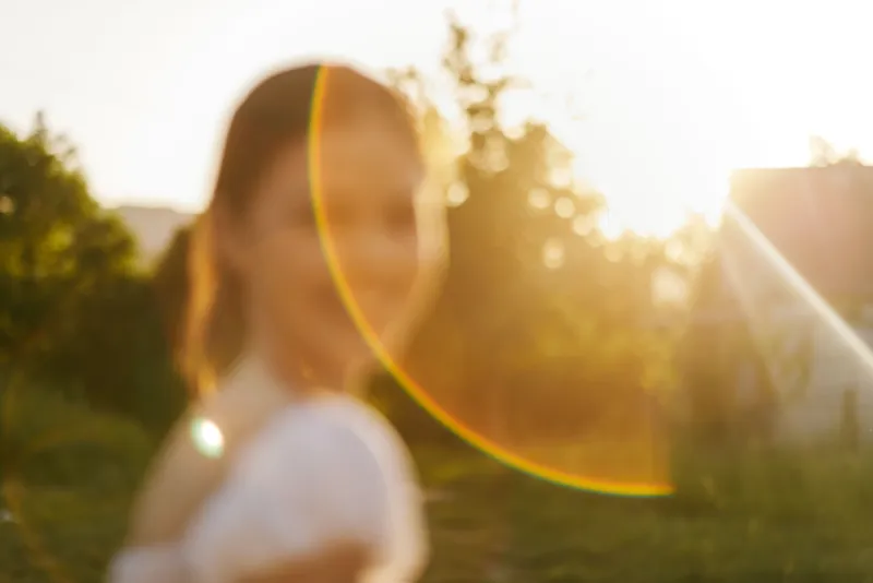 Soft sunlight illuminating a smiling woman in a garden setting, showcasing natural beauty and serenity in a vibrant outdoor atmosphere