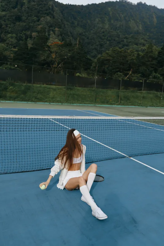 Young female tennis player enjoys a moment of relaxation on the court in white sportswear, displaying joy against a lush green background