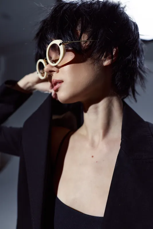 Stylish woman wearing round sunglasses and black jacket posing with confident expression in dramatic lighting