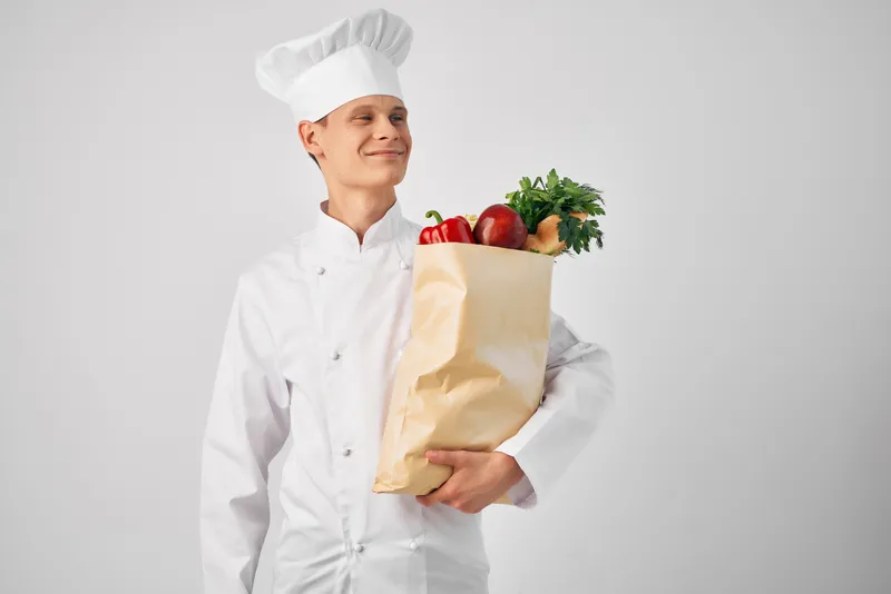 Мужчина в форме повара с пакетом продуктов работает и обслуживает