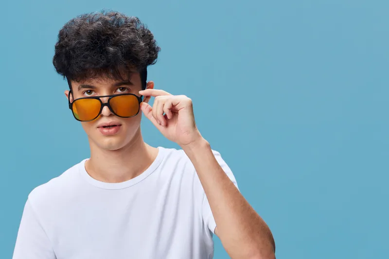 young man wearing white t-shirt and yellow sunglasses on blue background looking intrigued and curious expression with casual style