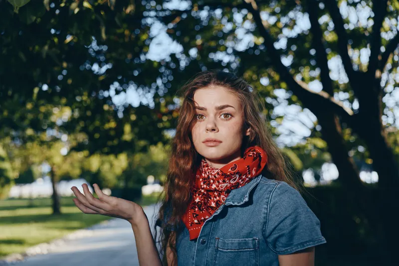 lifestyle woman in modern boho-western denim street style with red bandana, natural light, casual confidence, film color tones, outdoor park setting