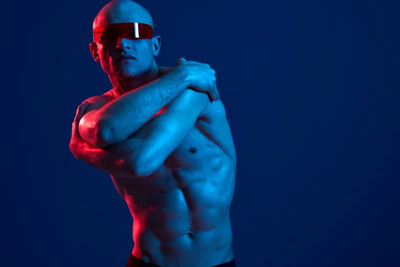 Athletic man posing confidently with futuristic sunglasses, showcasing a modern aesthetic in a vibrant blue and red color palette, radiating energy and style.