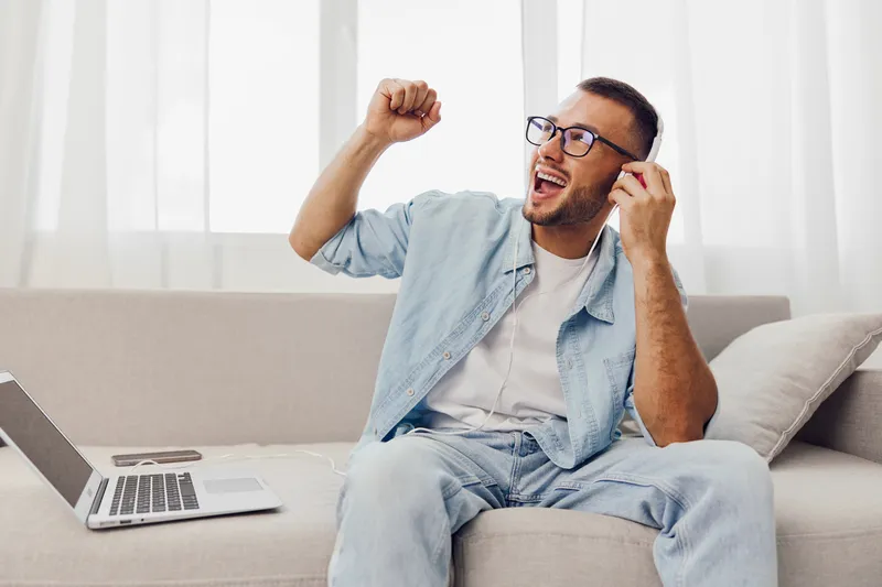 Enthusiastic man listening to music, enjoying a digital detox while relaxing on a couch. This moment highlights the importance of mental health and self-care.