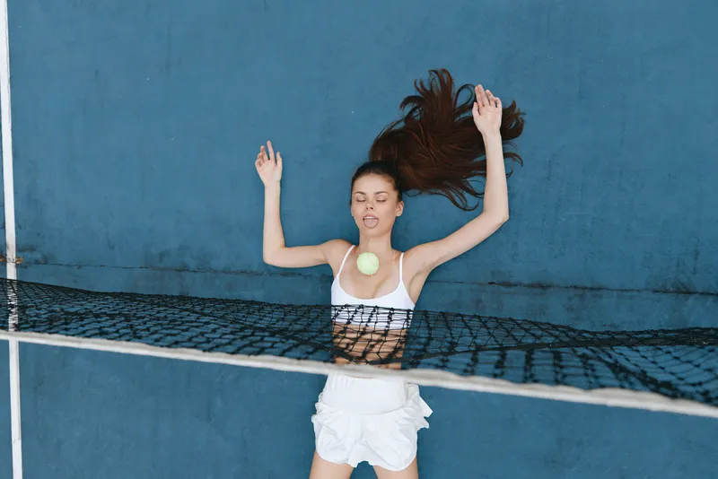 Young woman enjoying a swimming session with a tennis ball, wearing a white swimsuit and surrounded by blue water, capturing a refreshing summer vibe