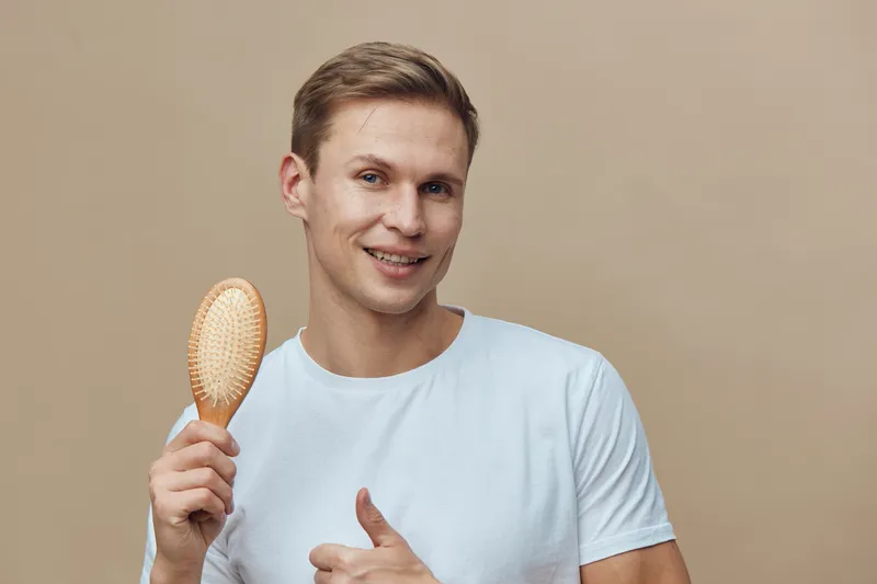 smiling young caucasian man in white t-shirt hold hairbrush show thumb up isolated on beige background digital detox mental health concept