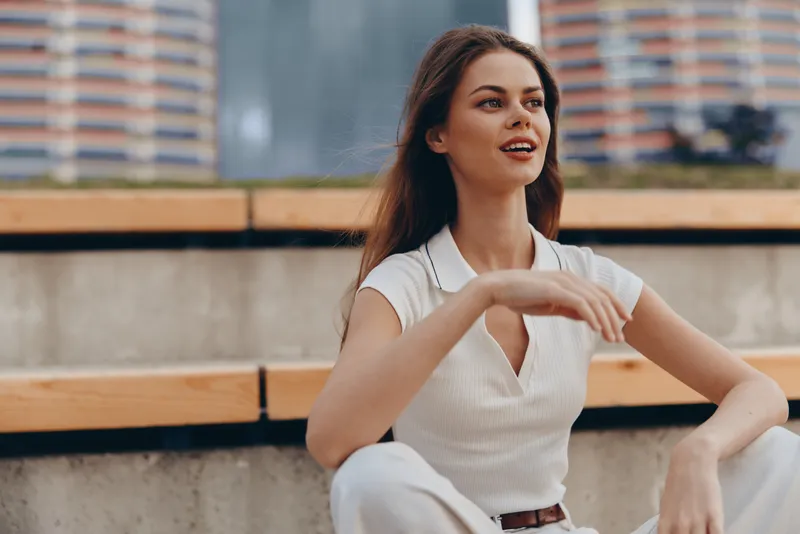 Confident woman with brown hair smiling outdoors in casual white outfit with urban background, natural light, and modern lifestyle concept