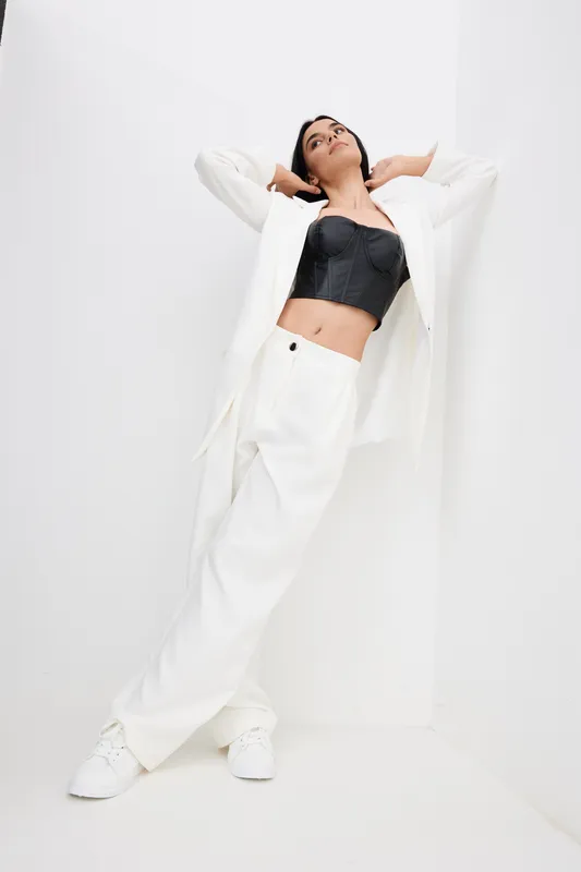 woman in white suit and black top posing stylishly against white wall, contemporary fashion, minimalistic background, casual and confident mood