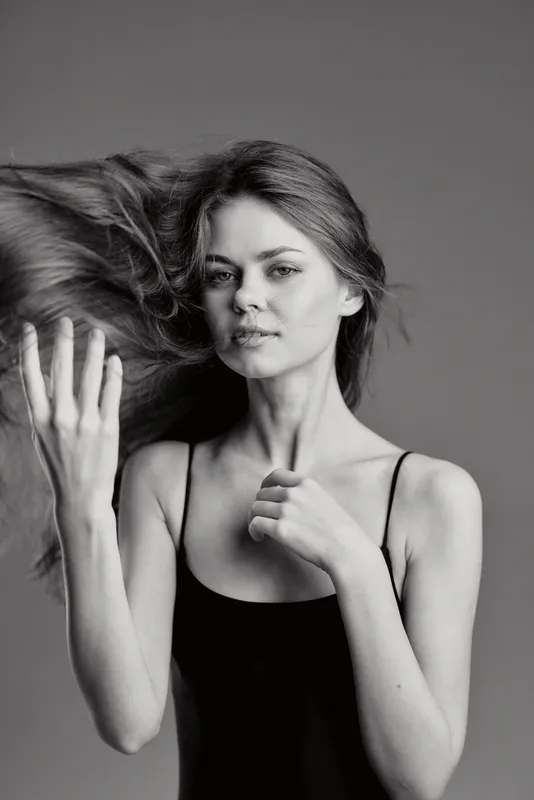 Black and white portrait of young woman with flowing hair in simple black dress against gray background