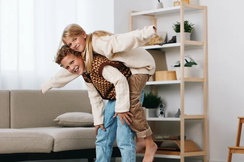 Playful couple shares a piggyback moment indoors, capturing joyful energy, trust, and affection in a bright living room with soft light and cozy furnishings.