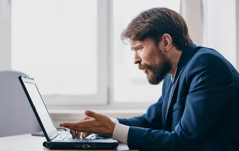 Мужчина в офисе сидит перед ноутбуком и работает