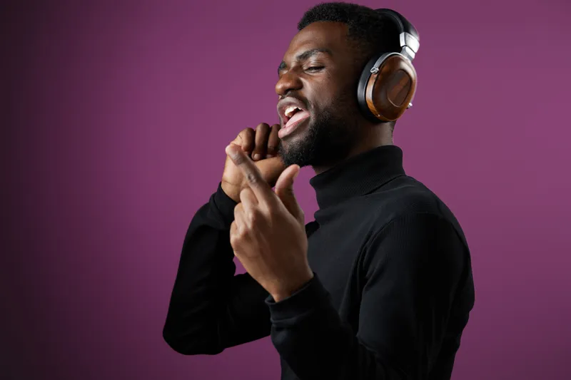 A young Black male enjoying music while singing passionately, wearing stylish headphones, against a vibrant purple background, showcasing a joyful and energetic vibe