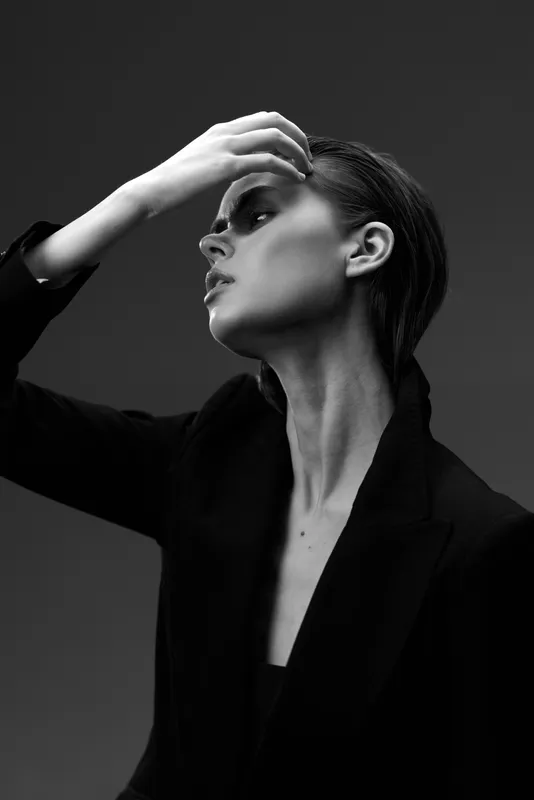Black and white portrait of a thoughtful woman in stylish blazer with dramatic lighting and elegant pose
