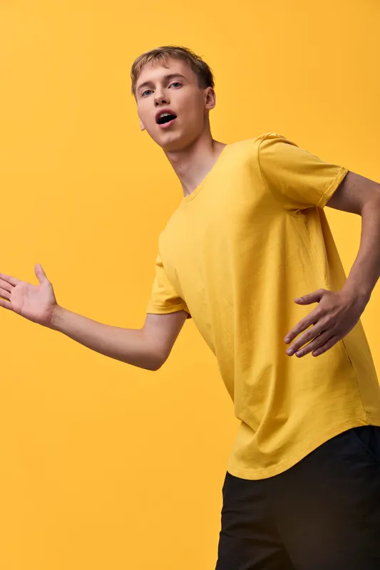 Energetic young man in a yellow tee moves against a matching backdrop, conveying excitement and motion for fashion, lifestyle, or sports themed projects in a studio setting