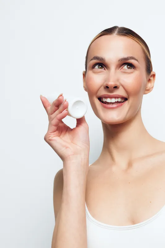 Young smiling woman with clear skin holds white cosmetic jar near face looks up happily isolated on white background beauty skincare concept natural fresh clean appearance