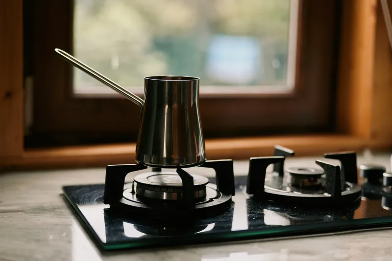 Coffee pot on a gas stove in a modern kitchen, steam rising as heat glows, capturing a focused warm cooking moment in a simple home setting