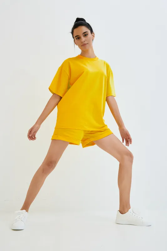young woman in bright yellow activewear stretching legs indoors, fitness, workout, casual style, white sneakers, minimalistic background, sporty look