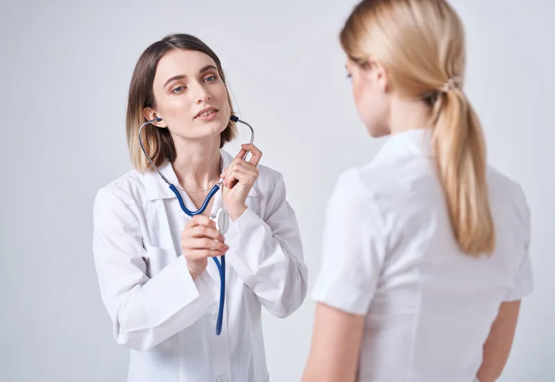 Врач в медицинском халате на светлом фоне и пациентка — блондинка