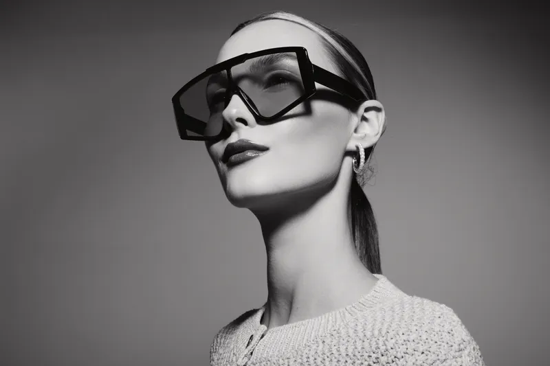 Portrait of white woman with pale skin wearing large black glasses and light sweater in studio light.