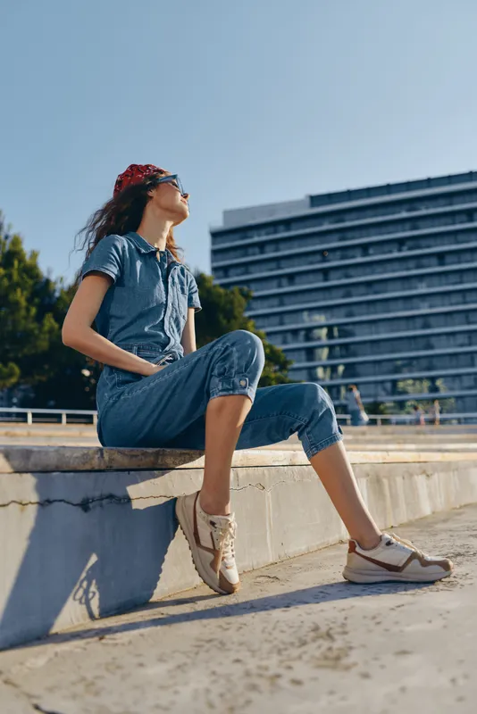 Lifestyle woman in modern boho-western denim street style with red bandana and casual shoes, enjoying sunny urban day with film color tones and relaxed mood.