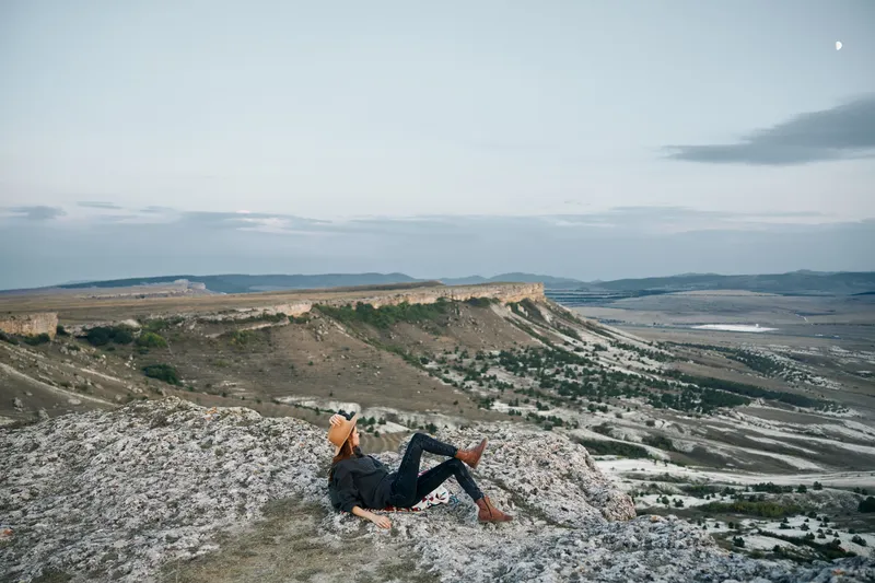 Безмятежная женщина на закате созерцает долину и горы, сидя на камне
