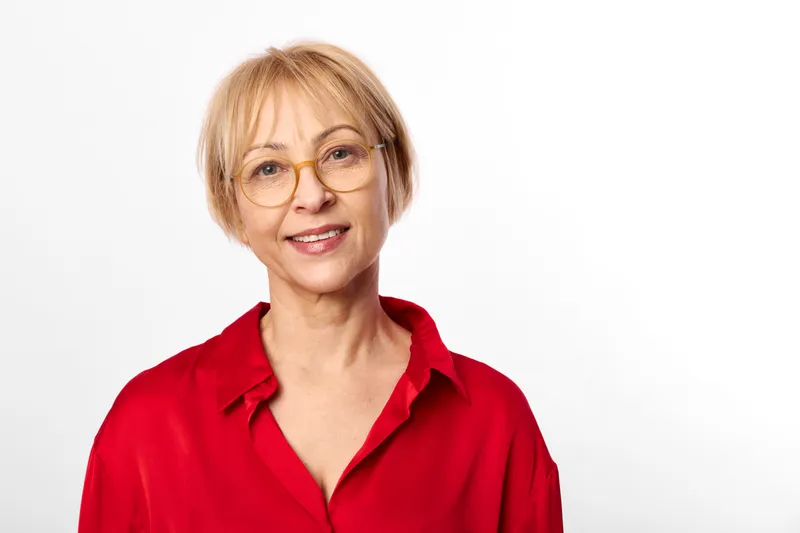 Senior woman portrait, glasses smile, red blouse in studio, white background, soft lighting, head and shoulders, calm mature female expression, confident posture