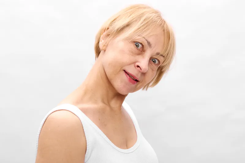 Blond woman portrait surprised closeup face headshot, light studio indoor gray neutral background, young female with short hair, relaxed playful expression, looking camera