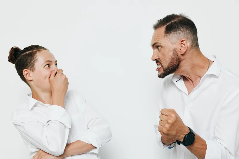 A tense business scene shows a professional man facing a colleague in a white studio, highlighting confrontation, strong emotion, and a decisive stance against a clean isolated background.