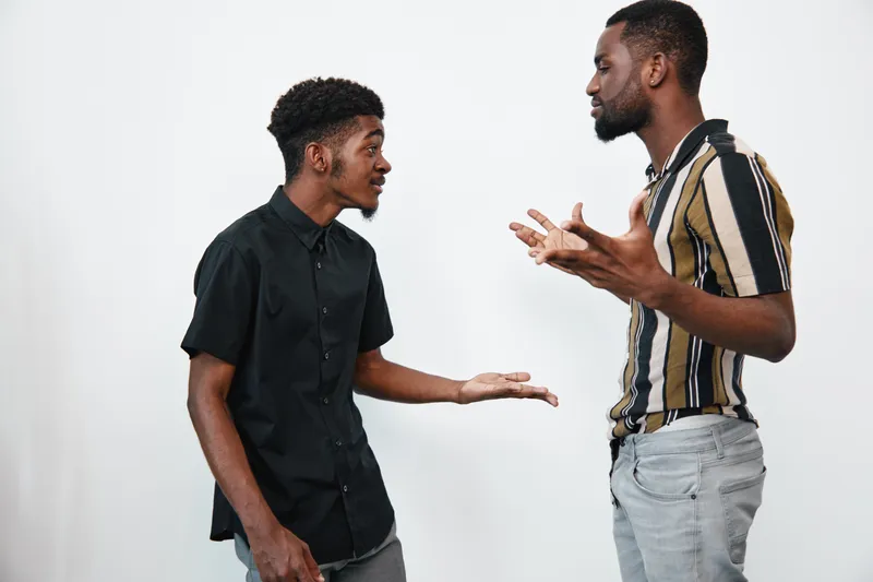 Two african american men with dark skin having a serious conversation in casual clothes on white background. Young black males discussing with expressive gestures indoors.