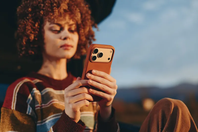 Woman lifestyle outdoors smartphone portrait curly hair selfie sunset relaxed expression holding phone in hands warm evening light blurred hills soft breeze natural colors casual moment
