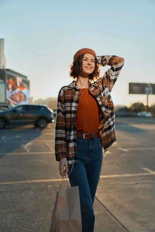 Woman shopping in urban parking lot at golden hour, candid smiling portrait conveying authenticity and mindful living, emotional storytelling with golden hour glow and relaxed lifestyle.