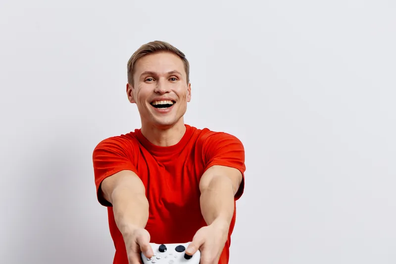 Smiling man in red t-shirt holding a game controller, expressing joy and excitement, isolated on plain white background, studio portrait, vibrant colors, casual style, leisure activity.