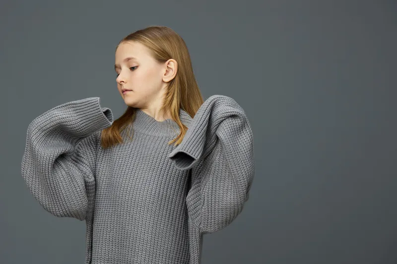 Stylish young model in a cozy gray oversized sweater with puff sleeves, showcasing a serene expression against a minimalist gray backdrop, perfect for fashion photography
