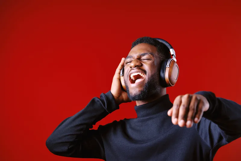 Young African man enjoying music with headphones on a vibrant red background, expressing joy and relaxation through music