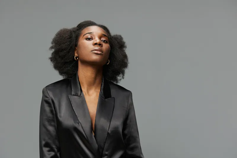 Elegant confident woman in black blazer against a neutral background, embodying professionalism and empowerment with natural afro hairstyle