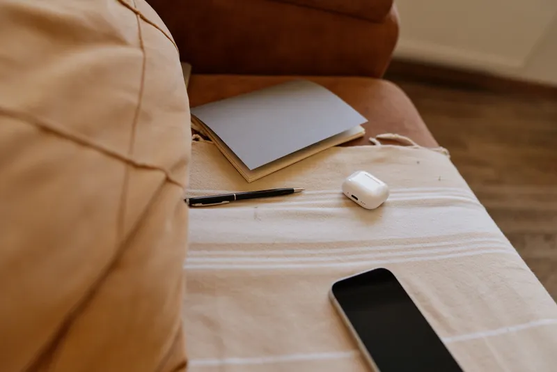 Woman relaxing at home on a sofa with a notebook and a smartphone, casual lifestyle scene, warm light, cozy textures, calm mood.