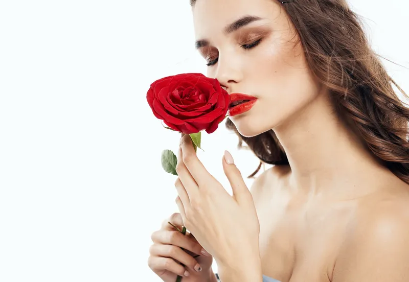 Очаровательная брюнетка с обнаженными плечами и ароматным цветком возле лица
