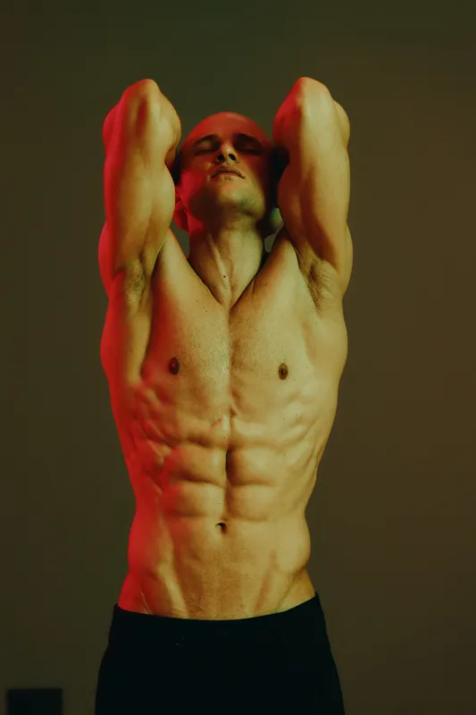 Muscular man striking a powerful pose, showcasing his toned body with dramatic lighting and shadows. This striking image captures strength and confidence.