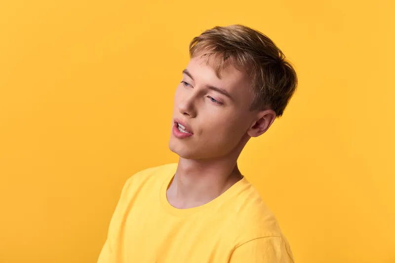 Young man wearing a yellow shirt against a vibrant yellow backdrop, thoughtful expression, casual studio shot highlighting mood, color harmony, and soft lighting for lifestyle imagery