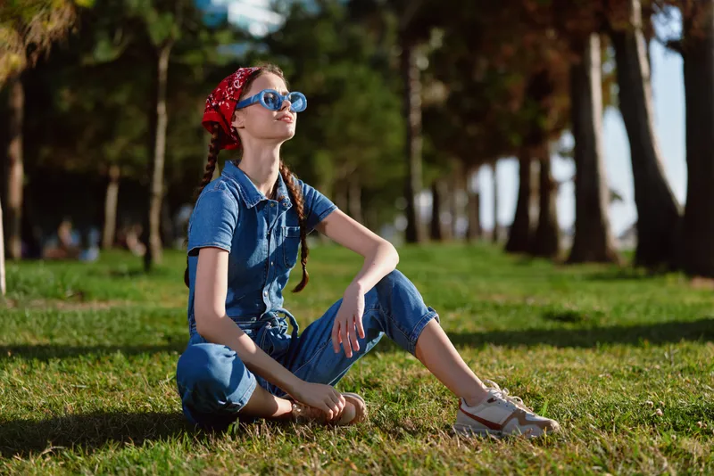 lifestyle woman in modern boho-western denim street style sits on grass with relaxed posture under warm natural light, film color effect enhances casual mood