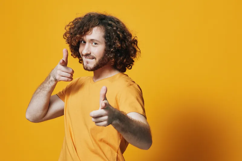 Young man with curly hair in a yellow t shirt against a bright yellow background, exuding confidence and positivity, perfect for cheerful themes