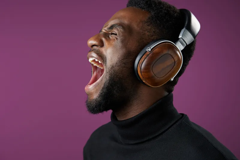 Young Black man enjoying music with stylish headphones, expressing emotions in a vibrant purple background, showcasing passion for sound
