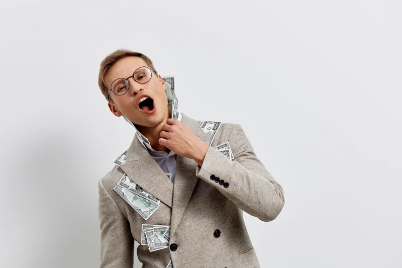 young caucasian man wearing glasses biting money banknotes in coat happy excited smile financial success wealth concept