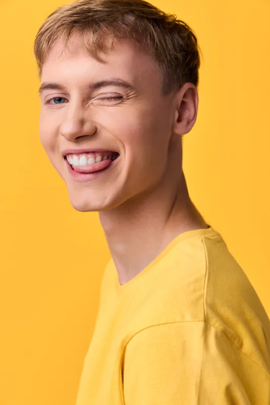 Close up of a cheerful, casual figure with a bright yellow shirt, a playful wink and warm smile, capturing a positive mood ideal for lifestyle branding and youthful campaigns