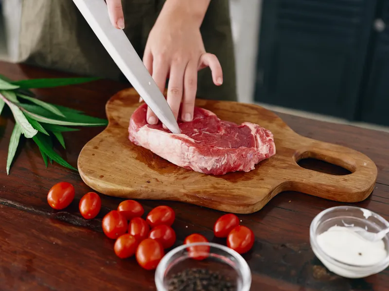 Женщина с ножом в руке нарезает свежее стейковое мясо для жарки на кухне