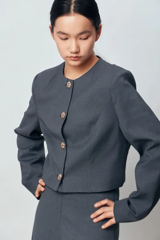 Young Asian woman in gray formal jacket and skirt stands with hands on hips looking down on light background. Professional attire with buttons and neat hairstyle in studio portrait.