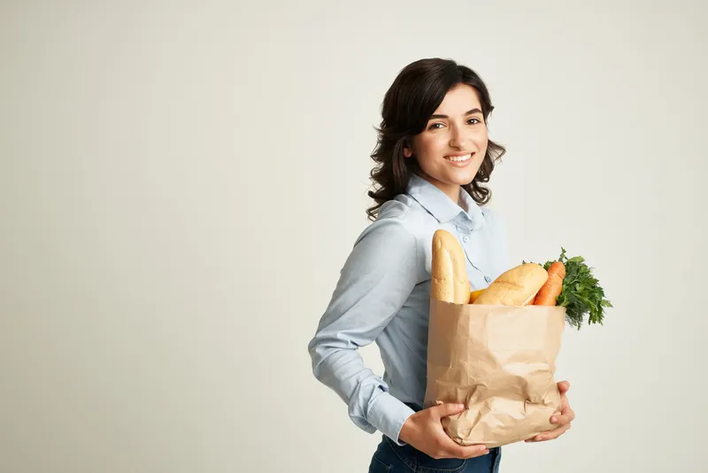 Милая брюнетка с продуктовой упаковкой для доставки из супермаркета на светлом фоне